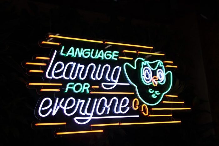 Una imagen de luces de neón con el logotipo del búho de Duolingo y el texto "Aprendizaje de idiomas para todos".
