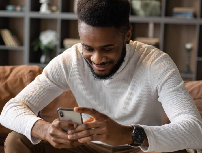 Una imagen de un hombre sonriendo mientras mira su teléfono, presumiblemente disfrutando de algo en la pantalla.